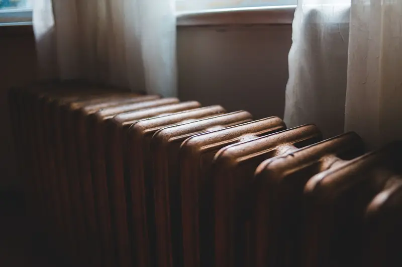 An old cast-iron radiator under a curtained window.