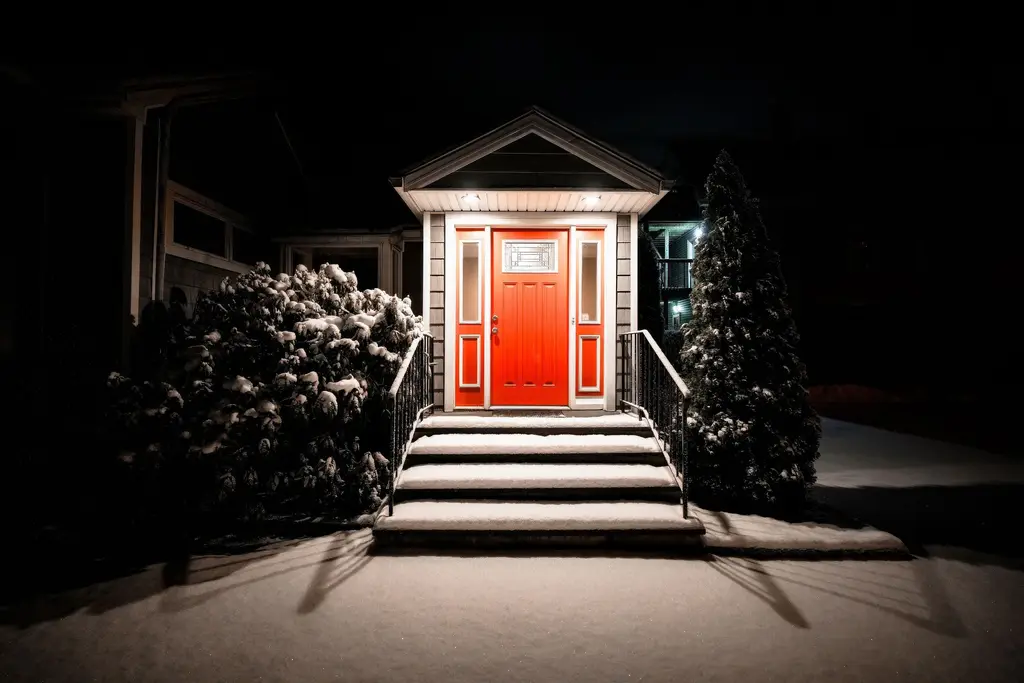 Lit front door and snowy steps of a house at night.