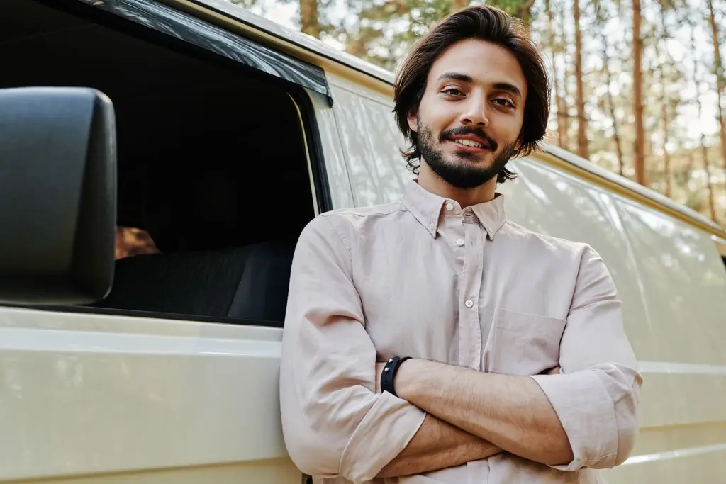 Smiling plumber leaning on his white service van, arms crossed.